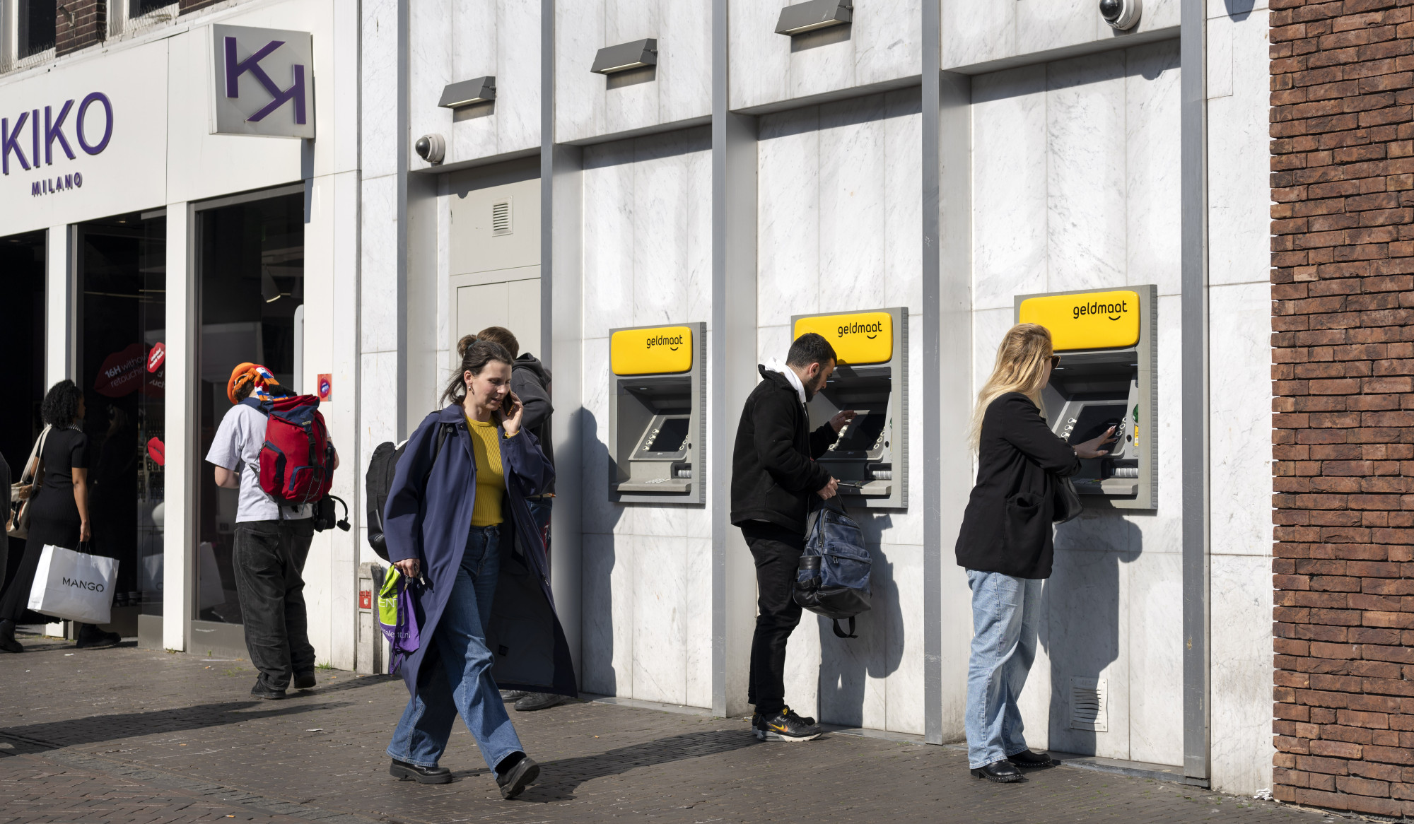 Twee mensen bij rij pinautomaten en voorbijgangers.jpg Twee mensen bij rij pinautomaten en voorbijgangers.jpg